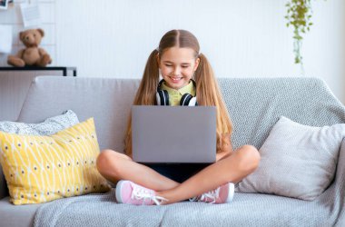 Çevrimiçi sohbet. Koltuğunda, boynunda kulaklıklarla dizüstü bilgisayarla oturan neşeli kızın ön portresi.