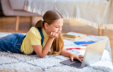 Gülümseyen kız öğrenci dizüstü bilgisayarını kullanarak evde ders çalışıyor.