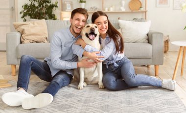 Gerçek Aşk Konsepti. Mutlu adam ve kadın Golden Retriever 'larına sarılıyorlar. Evde yerde oturuyorlar.