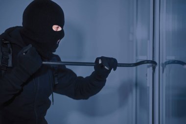 Davetsiz giriş kavramı. Gizlenmiş hırsızın yan görünüm portresi. Ev veya ofis kapısı levyeyle kırılıyor.