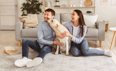 Samimi Duygular. Genç, sevgi dolu bir aile köpekle oynuyor yerde oturuyor, Labrador sahibinin yüzünü kokluyor.