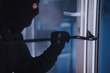 Vandalizm Konsepti. Siyah kar maskesi ve eldiven giyen davetsiz misafirin levyeyle ev kapısını kırması.