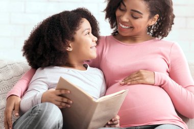 Educational Activities. Happy African Mom And Her Little Daughter Reading Book Together, Sitting On Couch In Living Room At Home, Free Space