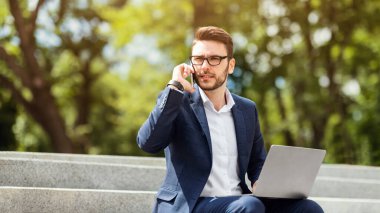 Genç CEO bilgisayarda dokümanları karıştırıyor ve şehir parkındaki merdivenlerde telefon görüşmesi yapıyor.