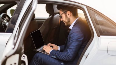 Genç iş adamı dizüstü bilgisayar kullanıyor. Aracının arka koltuğunda boş ekran var. Tasarım için model alıyor. Panorama