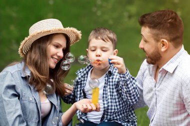 Ailesiyle piknikte eğlenen sevimli çocuk parkta sabun köpüğü üflüyor. Panorama