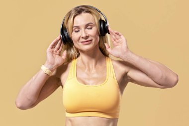 COVID-19 salgını sırasında evde tek başına müzik dinlemenin tadını çıkar. Spor kıyafetleri içinde gözleri kapalı, modern kulaklıklara dokunan kaslı yetişkin bir kadın.