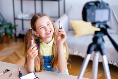 Gençler İçin Telafi. Gülümseyen kız, internet kanalı için kameraya iki ruj gösteriyor.