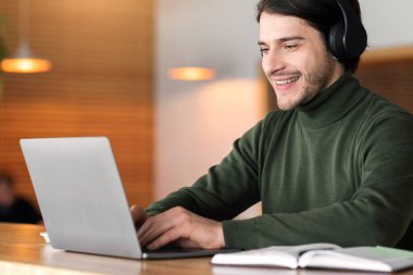 Kablosuz kulaklıklı genç adam kafede dizüstü bilgisayarda çalışıyor, eğitim online konsept, boş alan