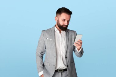 Millennial ofis çalışanı mavi arka planda akıllı telefondan iletişim kuruyor.