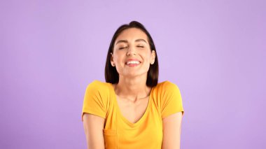 Olumlu duygular. Kapalı gözlerle gülümseyen neşeli bayan, Pastel mor stüdyo duvarında izole edilmiş, afiş