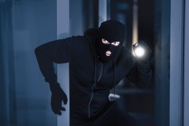 Siyah kar maskeli sinsi bir suçlu gece meşale kullanarak pencereden ya da camdan içeri sızıyor.