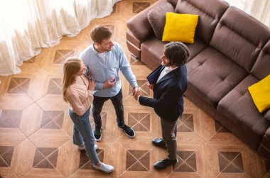 Mutlu evli çift ve emlakçı ev içi emlak anlaşması yaptıktan sonra el sıkışıyor.