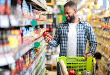 Süpermarketteki müşteri. Siyah adam market alışverişi yapıyor. Araba ile ayakta duruyor. Kapalı alanda yiyecek seçiyor. Afro-Amerikalı Adam Gıda Mağazasından alışveriş yapıyor. Seçici Odaklanma, Boşluğu Kopyala