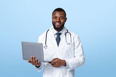 Karantina sırasında online danışmanlık. Dost canlısı Afrikalı Amerikalı doktor elinde dizüstü bilgisayarla beyaz stüdyo geçmişini araştırıyor.
