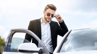 Resmi giyimli ve güneş gözlüklü ciddi bir CEO modern şehrin şehir merkezi olan Panorama 'da arabasına biniyor.