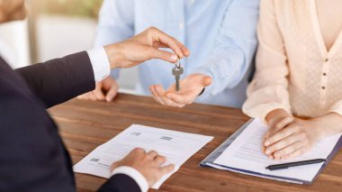 Emlakçı, masada emlak anlaşması imzaladıktan sonra ev anahtarını genç çifte veriyor.