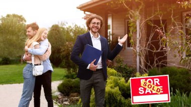 Gülümseyen ev temsilcisi ve mutlu çift yeni evlerinin bahçesinde kucaklaşıyorlar.