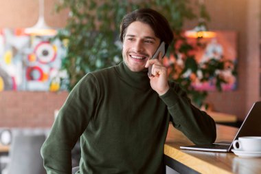 Cafe 'de dizüstü bilgisayarla çalışan yakışıklı bir adam müşterilerle telefonda konuşuyor.