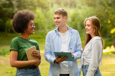 Üniversite öğrencileri derslerden sonra kampüste dinleniyorlar, ders kitaplarını tutuyorlar, sohbet ediyorlar ve birbirlerine gülümsüyorlar.