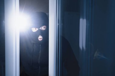 Soygun Konsepti. Bilinçli maskeli kötü adam pencereden ya da camdan içeri sızıyor, karanlıkta meşale kullanıyor.