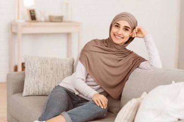 Modern tevazu. Türbanlı güzel bir Arap kızın portresi evdeki koltukta dinleniyor, kameraya gülümsüyor, boş yer var.