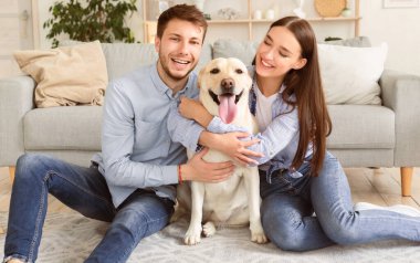Beraberlik kavramı. Heyecanlı arkadaşlar oturma odasında evcil hayvanlarıyla oynuyorlar, kameraya bakıyorlar.