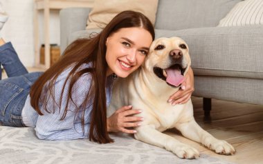 En iyi arkadaş. Modern dairede yerde uzanmış kameraya bakarak mutlu köpeği kucaklayan güzel bir kızın portresi.