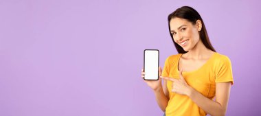 Yeni bir şey dene. Cep telefonunu işaret eden mutlu kız reklam için beyaz beyaz ekranlı, mor duvarlı.