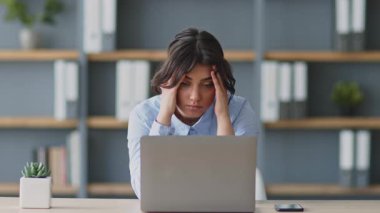 Odaklanmış genç bir kadın, evinde online olarak ders veriyor. Kitaplıklarla çevrili bir masada otururken bir dizüstü bilgisayar kullanıyor ve modern eğitim ortamını gösteriyor..