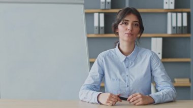 Genç bir kadın, iyi organize edilmiş bir ev ofisinden online ders veriyor. Odaklanmış ve meşgul görünüyor, eğitim materyalleri ile donatılmış..