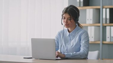 Kendini işine adamış genç bir kadın rahat evinde online özel ders veriyor. Modern eğitimi gösteren bir kulaklık takarak öğrencilerle laptopuyla iletişim kuruyor..