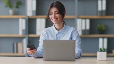 Genç bir kadın ev ofisinden online ders veriyor. Dizüstü bilgisayarına odaklanmış, kitaplıklarla çevrili, modern uzaktan eğitim yöntemlerini gösteriyor..