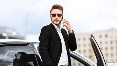 Şehir merkezinde arabasının yanında cep telefonuyla konuşan başarılı bir iş sahibi.