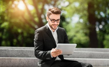 Şehir parkında öğle arasında tablet bilgisayarla çalışan pozitif şirket çalışanı.