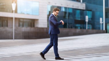 Şehir merkezinde yürüyen ve saatine bakan ciddi bir işyeri sahibi.