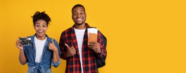 Tatil kavramı. Mutlu Afro-Amerikan çift fotoğraf makinesi ve seyahat biletleri sarı arka planda duruyor. Stüdyo Çekimi