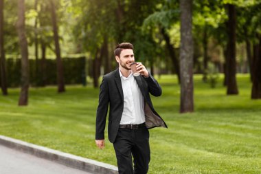 Güler yüzlü girişimci sabah kahvesini kağıt bardaktan içiyor şehir parkında yürürken