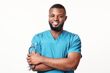 Steteskoplu gülümseyen Afrikalı genç doktor beyaz stüdyo arka planında poz veriyor.