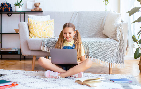 Девочка-подросток, сидящая с ноутбуком в позе лотоса на полу в уютной гостиной, пространство для копирования