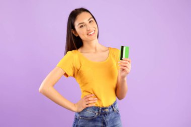 Kolay ödeme, bankacılık konsepti. Plastik kredi kartı tutan ve gösteren gülümseyen genç bayan modelin portresi, Pastel mor stüdyo arka planında izole edilmiş poz veren kadın. Ticaret ve Alışveriş.