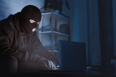 İsimsiz Kavram. Hacker siyah kar maskesi takıyor. Masada oturuyor. Özel bilgileri indiriyor.