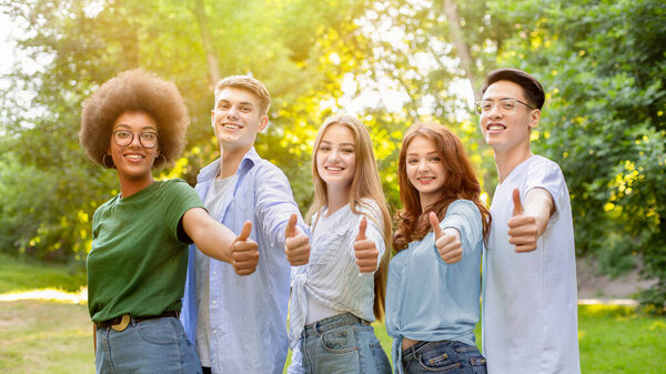 Group Of Multiethnic Teen Friends Standing Outdoors Showing Thumbs Up At Camera, Enjoying Spending Time Together, Free Space