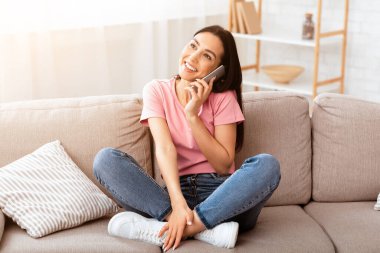 Arkadaş 'la hoş sohbetler. Dairesindeki bej koltukta oturan çekici, gülümseyen kız cep telefonuyla konuşuyor.