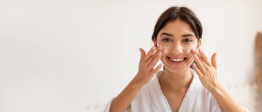 Orta Doğulu bir kadın, şımarık bir cilt bakımının bir parçası olarak yüzüne hidratasyon maskesi takıyor. Huzurlu bir spa ortamında rahatlamış ve neşeli görünüyor. Gençleşme ve kendine bakmayla ilgileniyor..