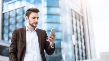 Kendine güvenen genç girişimci şehir sokaklarında cep telefonunu mesajlar için kontrol ediyor.