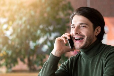 Arkadaşlarıyla akıllı telefondan konuşan kafeteryada kahve içen heyecanlı bir adam.