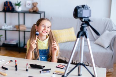 Makyaj yapan gülümseyen kız, kozmetik ürünleri incelemesi yapan, fırçalarını gösteren, gençleri ve yong derisini telafi eden, tripoddaki kameraya bakan. İnternet kanalı için video çeken kız