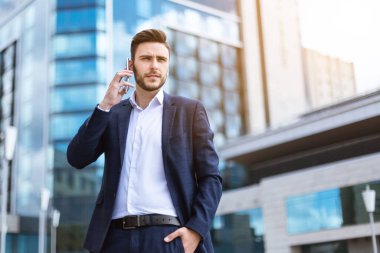 Çok katlı binanın önünde cep telefonuyla konuşan yakışıklı bir işletmeci.