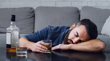 Alkol bağımlılığı. Sarhoş bir adam uyuyordu. Evde şişe ve camla masaya yaslanıyordu.